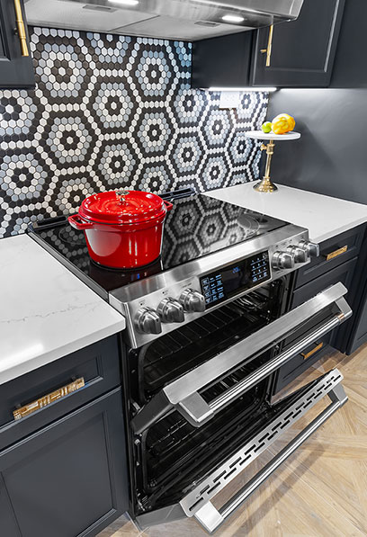 Contemporary kitchen design featuring a hexagon tile backsplash, stainless steel stove, and a red pot by Heather Toolin Designs in Austin, TX.