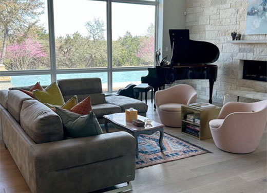 Contemporary living area with gray sectional, grand piano, and floor-to-ceiling windows.