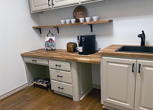 Modern utility room with white cabinetry, butcher block countertop, coffee station, and open shelving for storage.