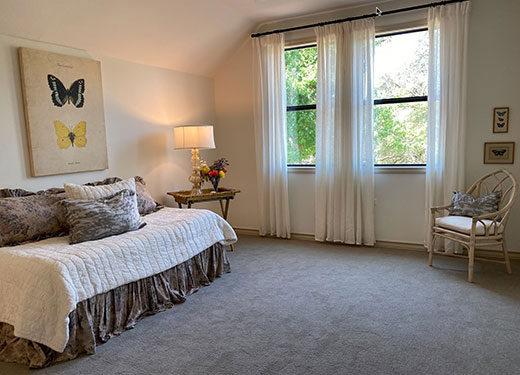 Bright bedroom with a daybed, butterfly wall art, and large windows, offering a serene and airy ambiance.