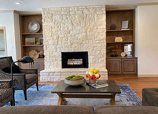 Living room with a stone fireplace, built-in wooden shelves, and a cozy seating area with a blue rug.