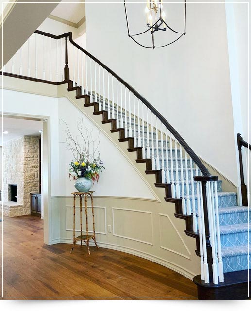 Elegant staircase with dark wood railing, white spindles, and a floral arrangement on a tall side table.