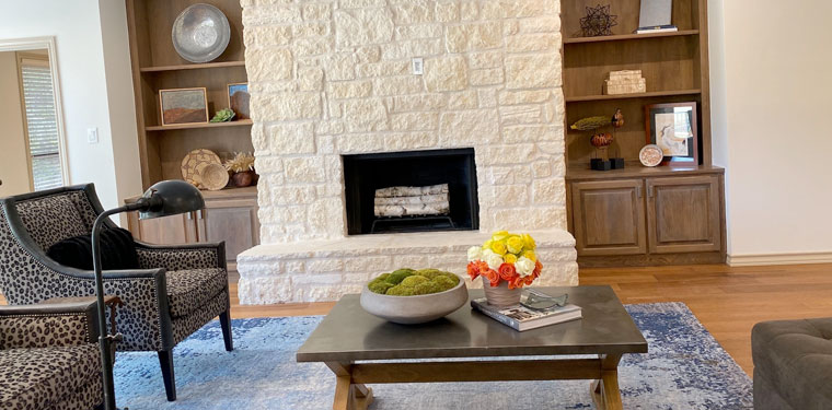 Cozy living room with stone fireplace, built-in shelves, and blue rug.